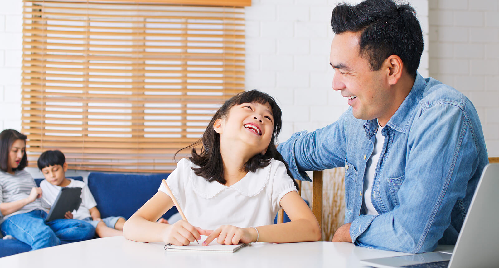 Nuori tyttö hymyilee isälleen tehdessään läksyjä.