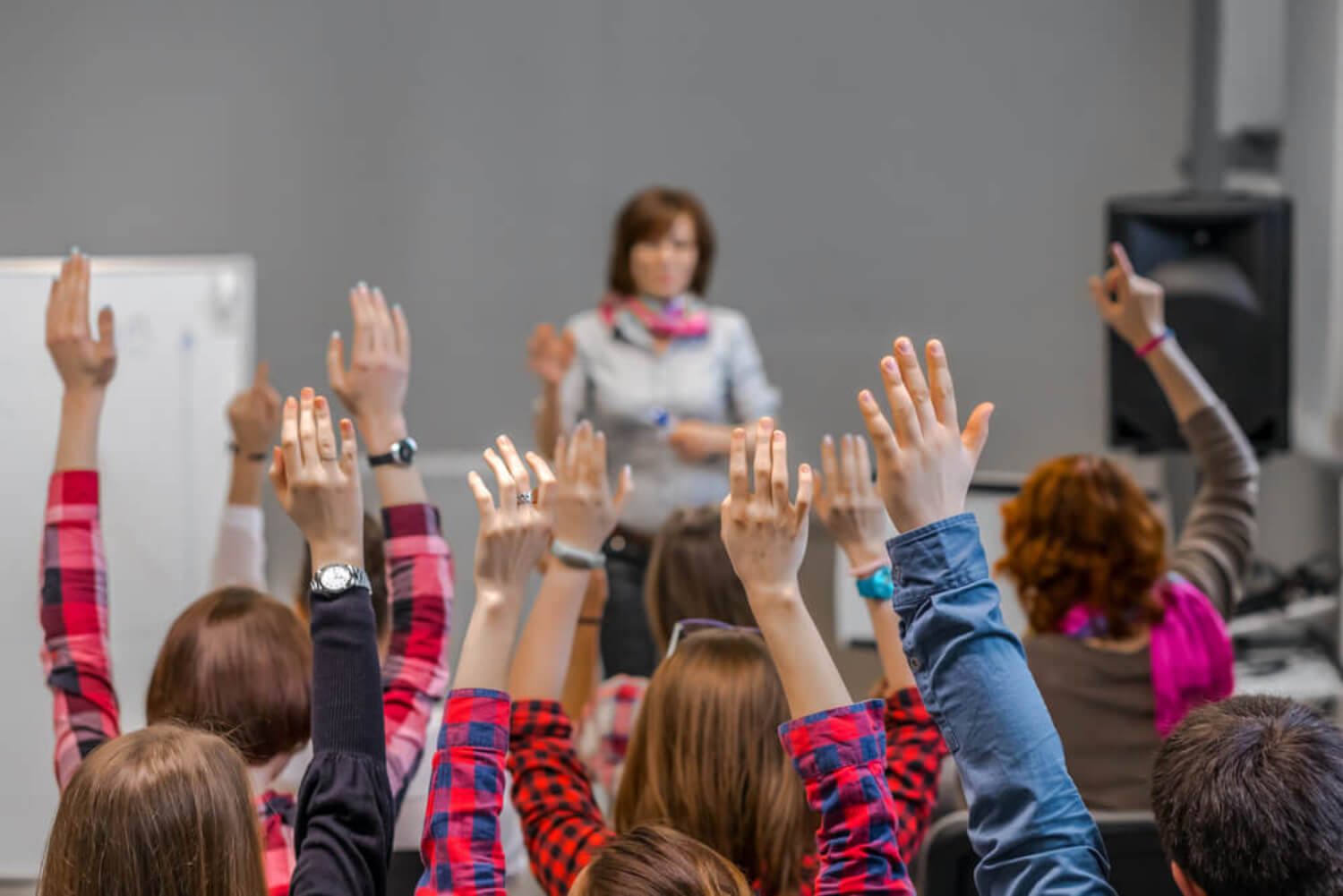 Des élèves en classe qui lèvent la main. 