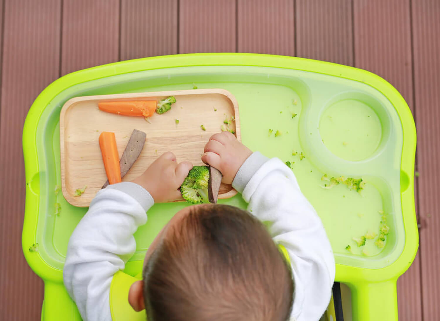 A baby eating soft foods with his hands.