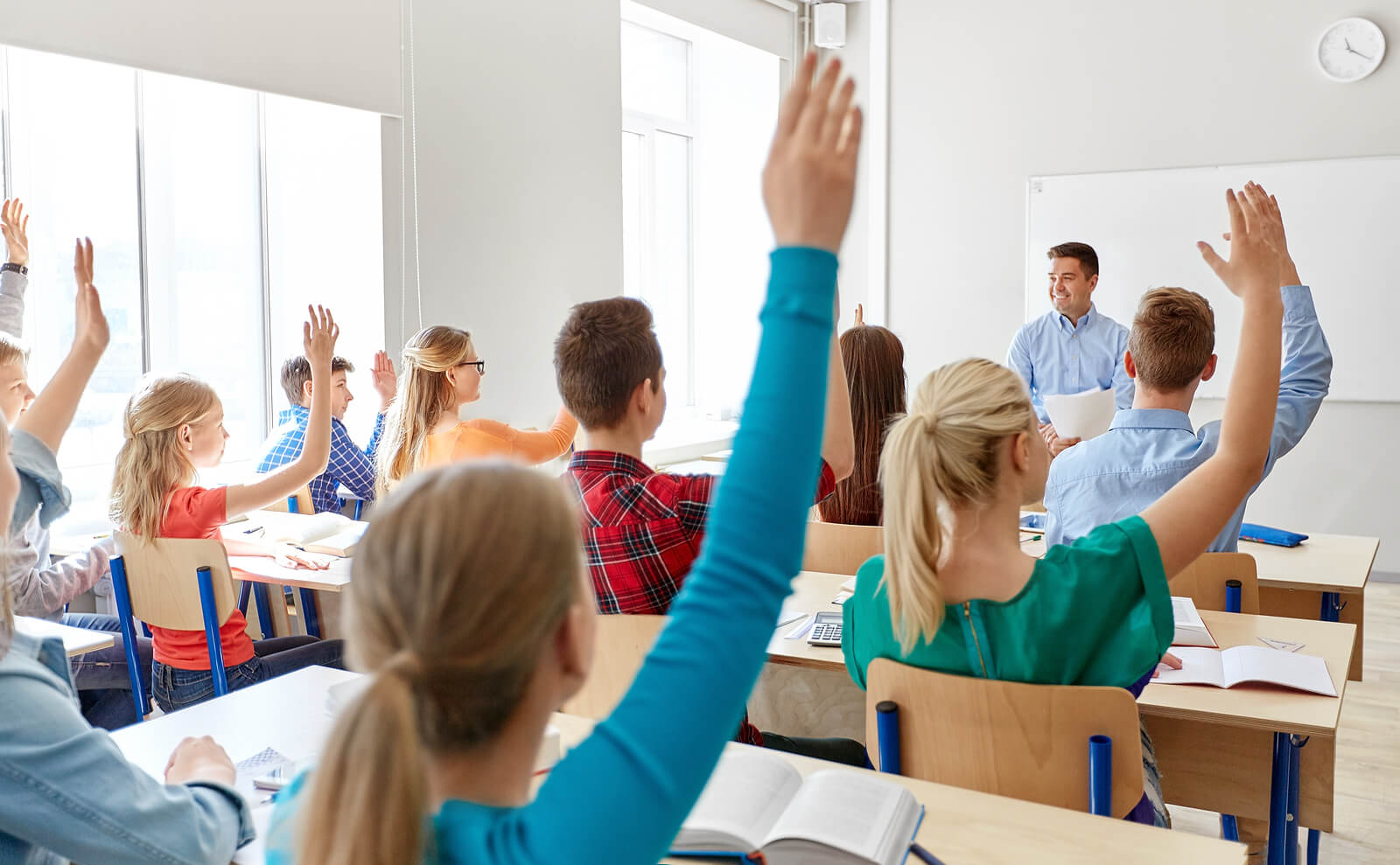 Gli studenti con le mani alzate per rispondere all'insegnante in classe.