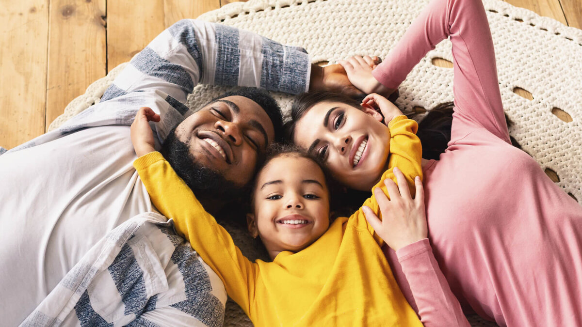 Familia feliz tumbada en el suelo mientras se dan un abrazo.