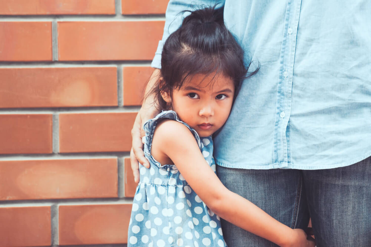 Niña con miedo abrazada a la pierna de su padre.