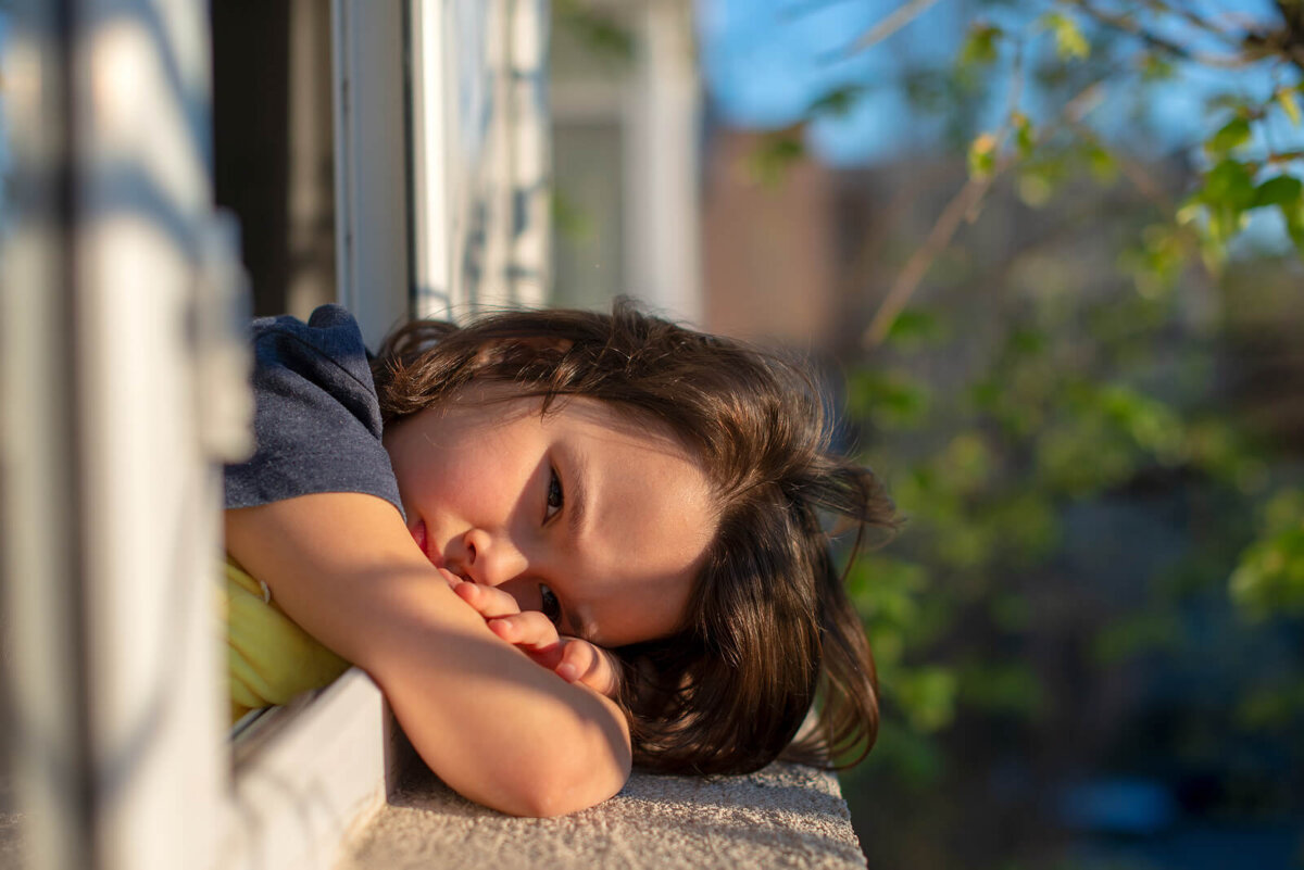 Niña asomada en la ventana triste porque no para de quejarse.