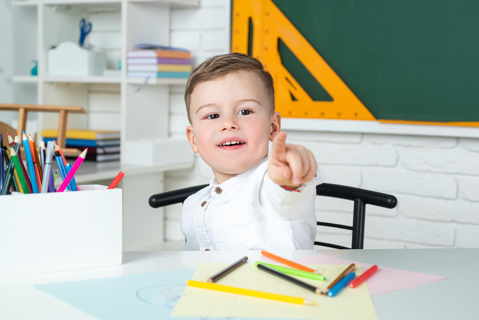 Un enfant à l'école devant une feuille avec des crayons.