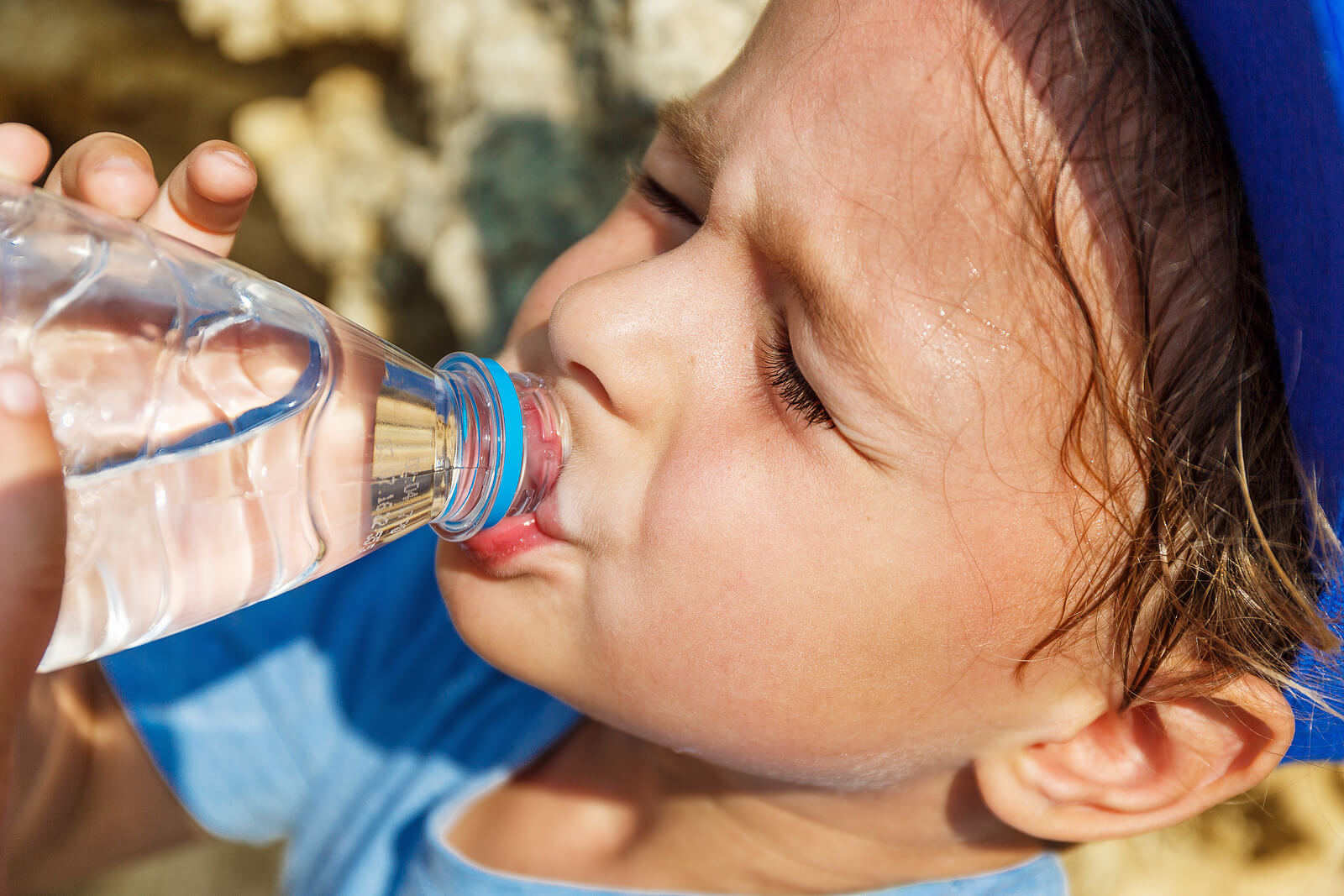 A boy drinking water because he's sweating a lot.