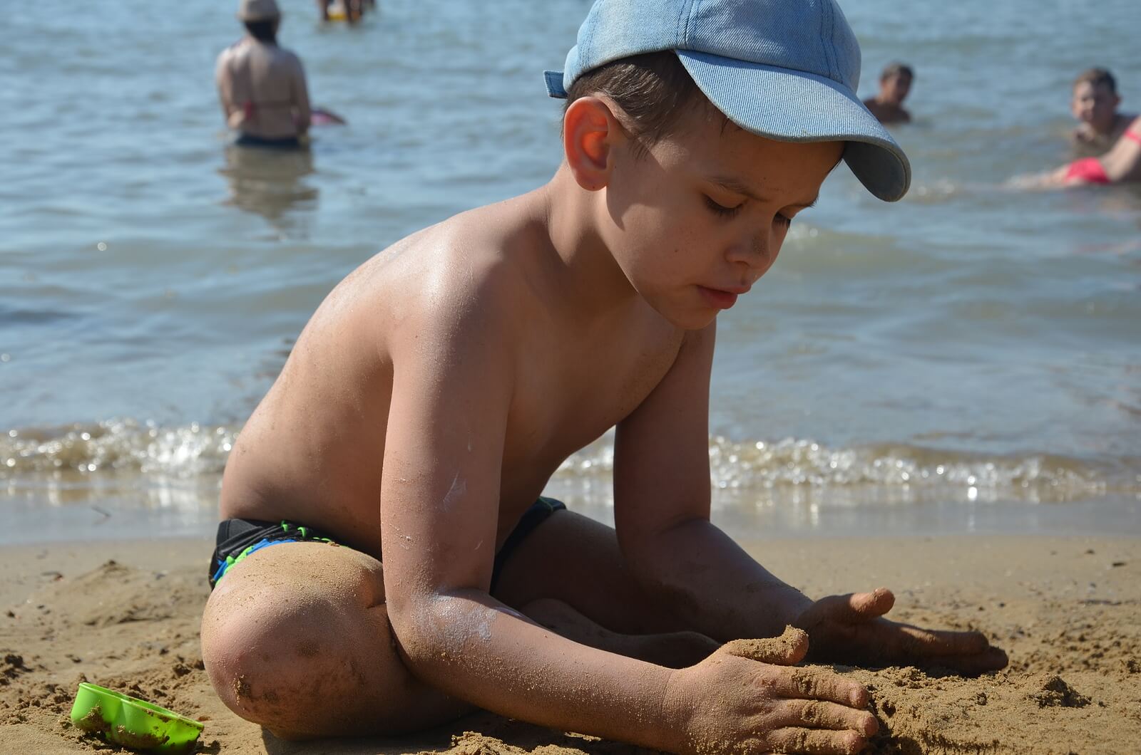 Niño en la playa haciendo un castillo de arena con la vigilancia de sus padres para evitar el ahogamiento en niños.