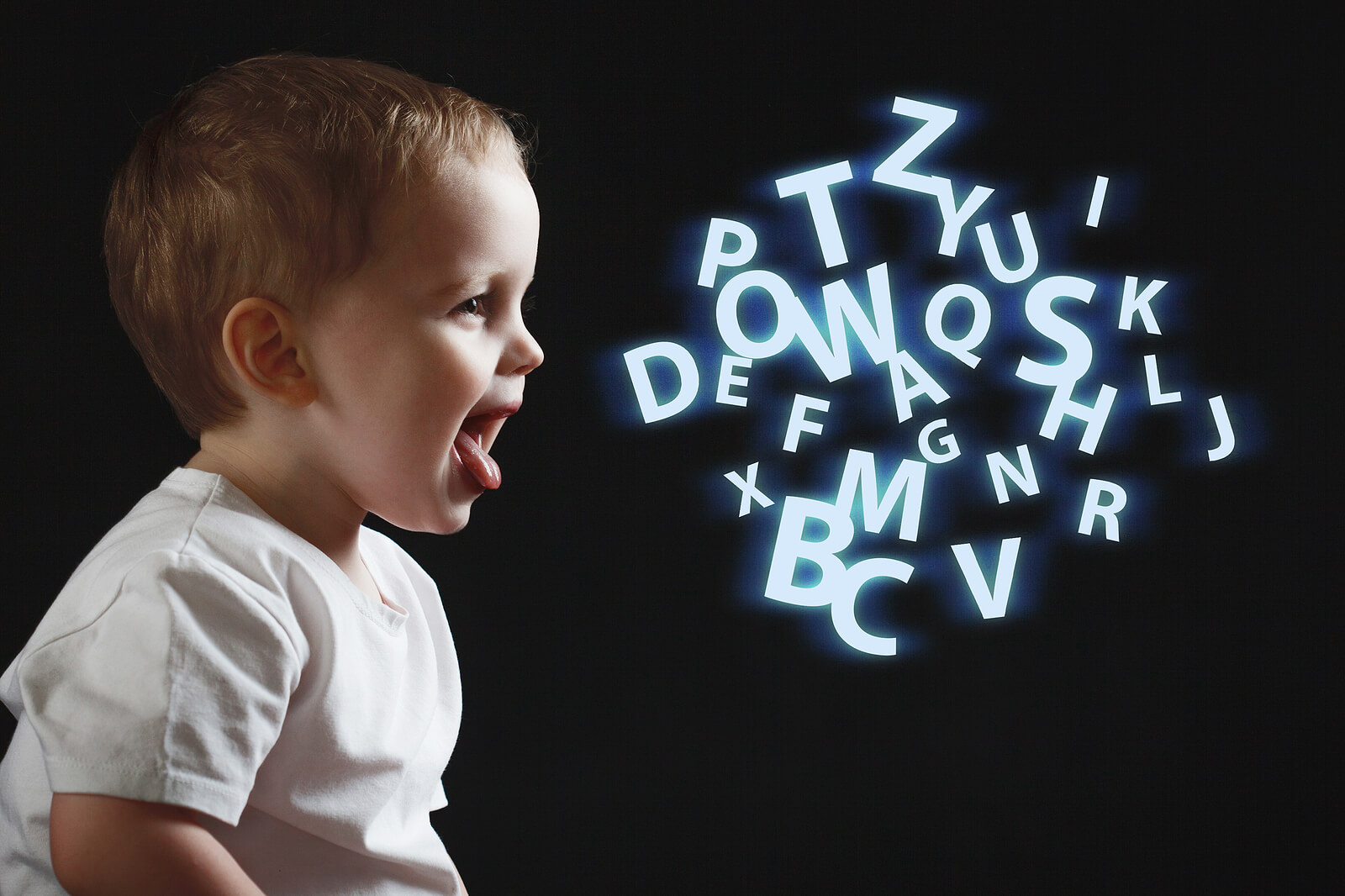 Ett litet barn talar med bokstäver som svävar i luften.