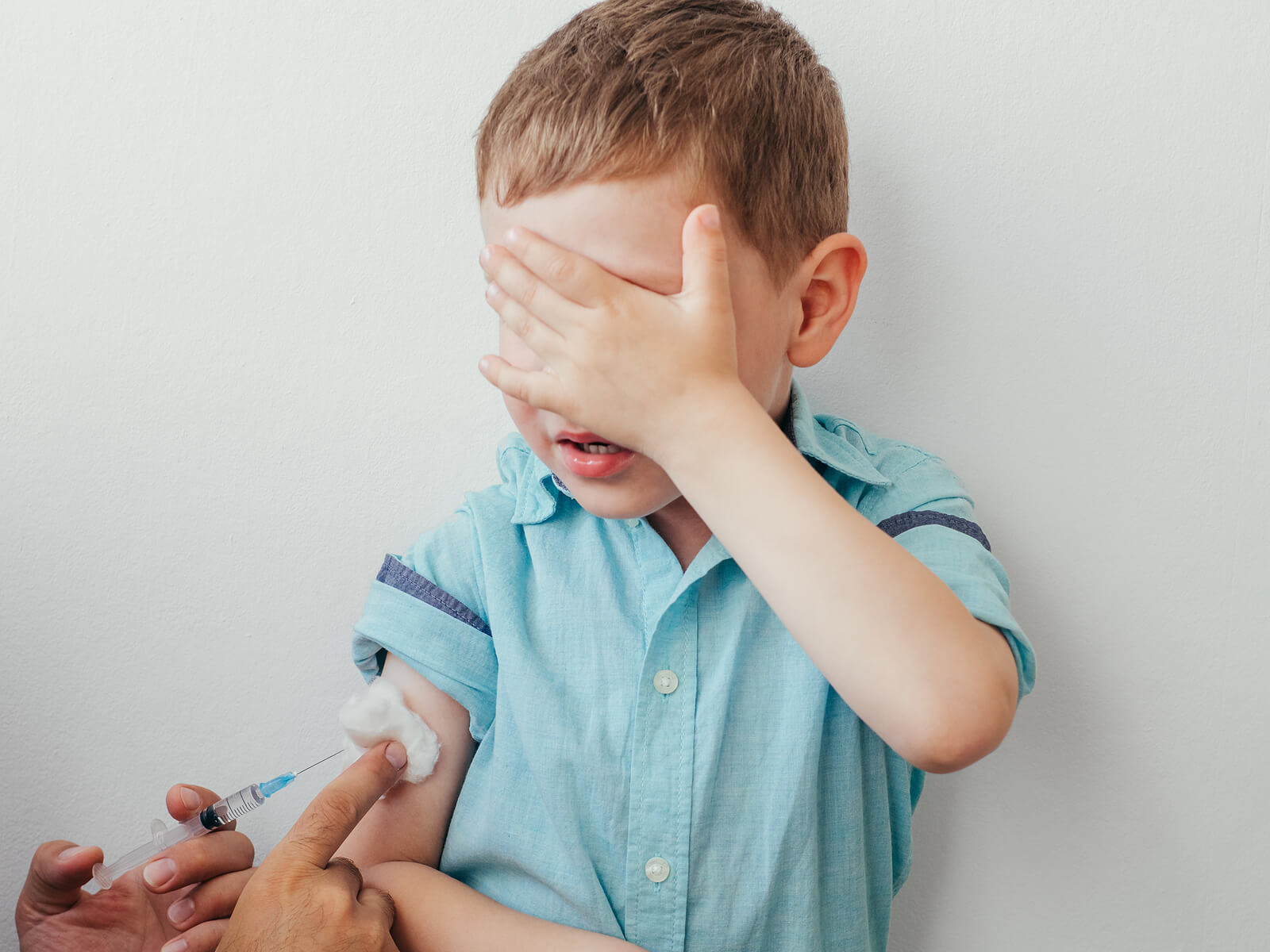Niño en el pediatra tapándose la cara porque tiene miedo mientras le vacunan.