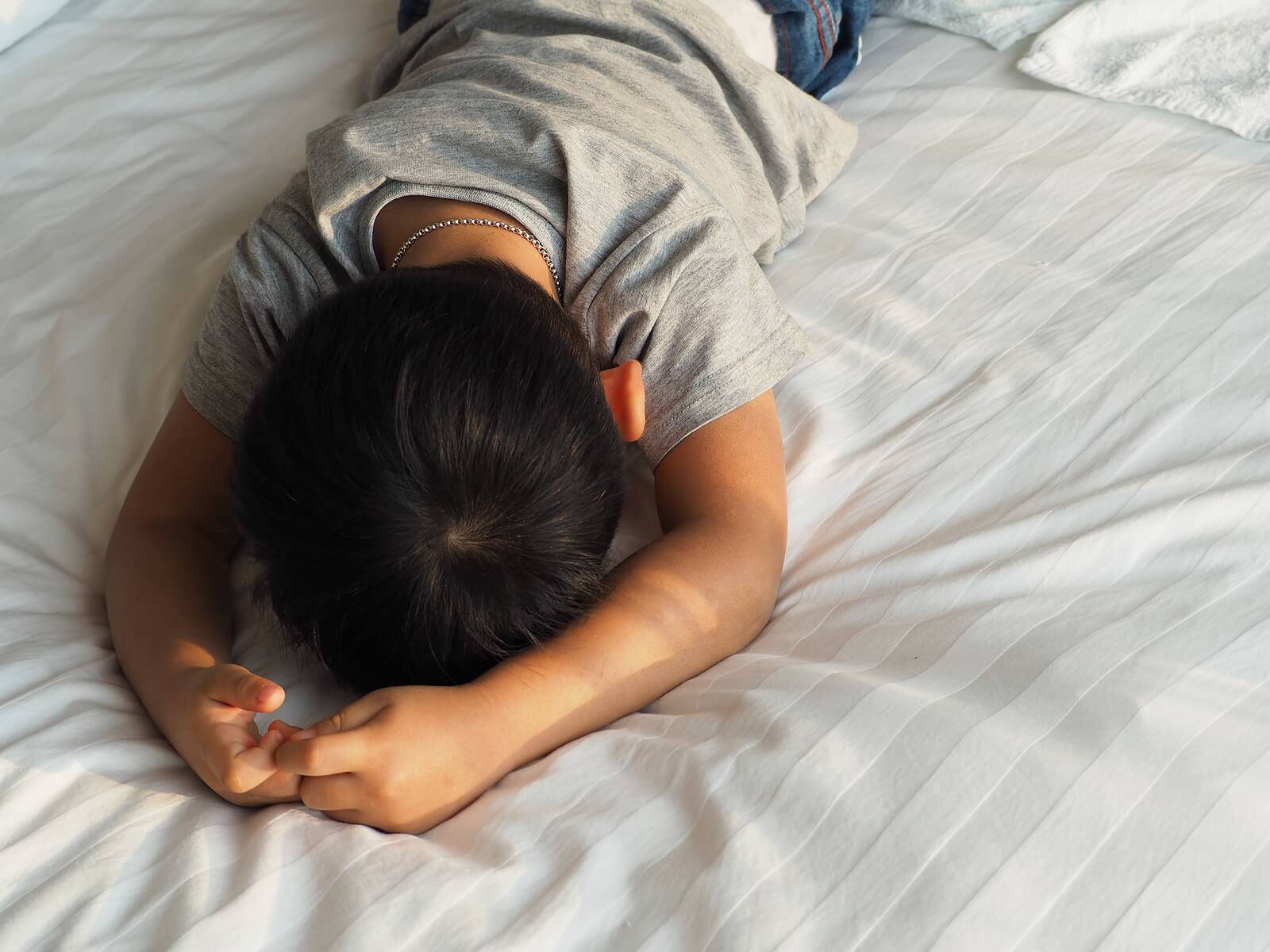 Niño con problemas de autorregulación tumbado en la cama mientras sufre una rabieta.