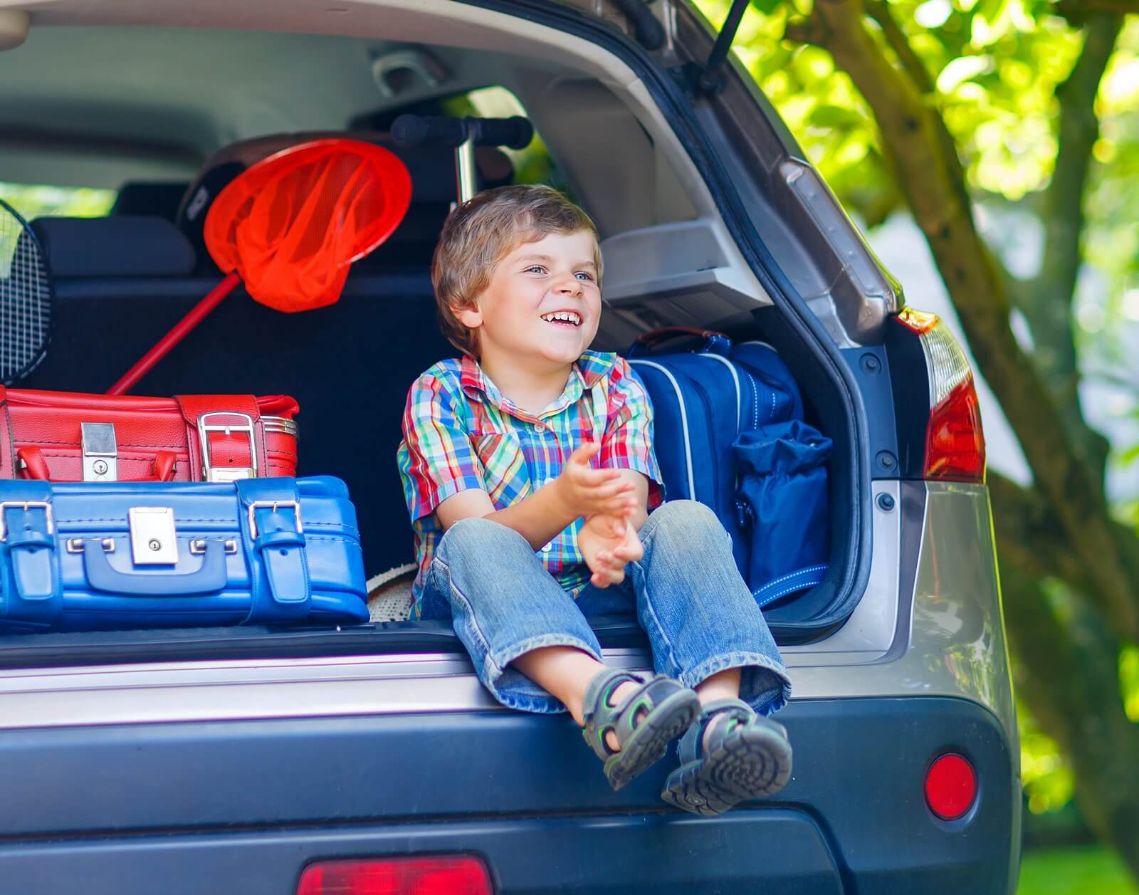 Niño sentado en el maletero del coche antes de hacer un viaje largo con sus padres.