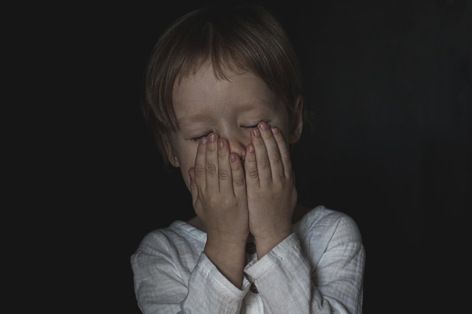 Niño con miedo a la oscuridad tapándose la cara con las manos.