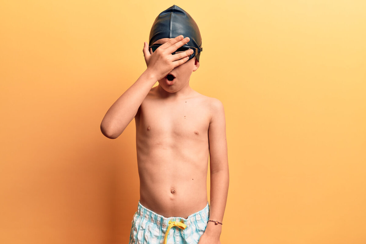 Niño con un gorro y gafas de piscina tapándose los ojos porque tiene hidrofobia.