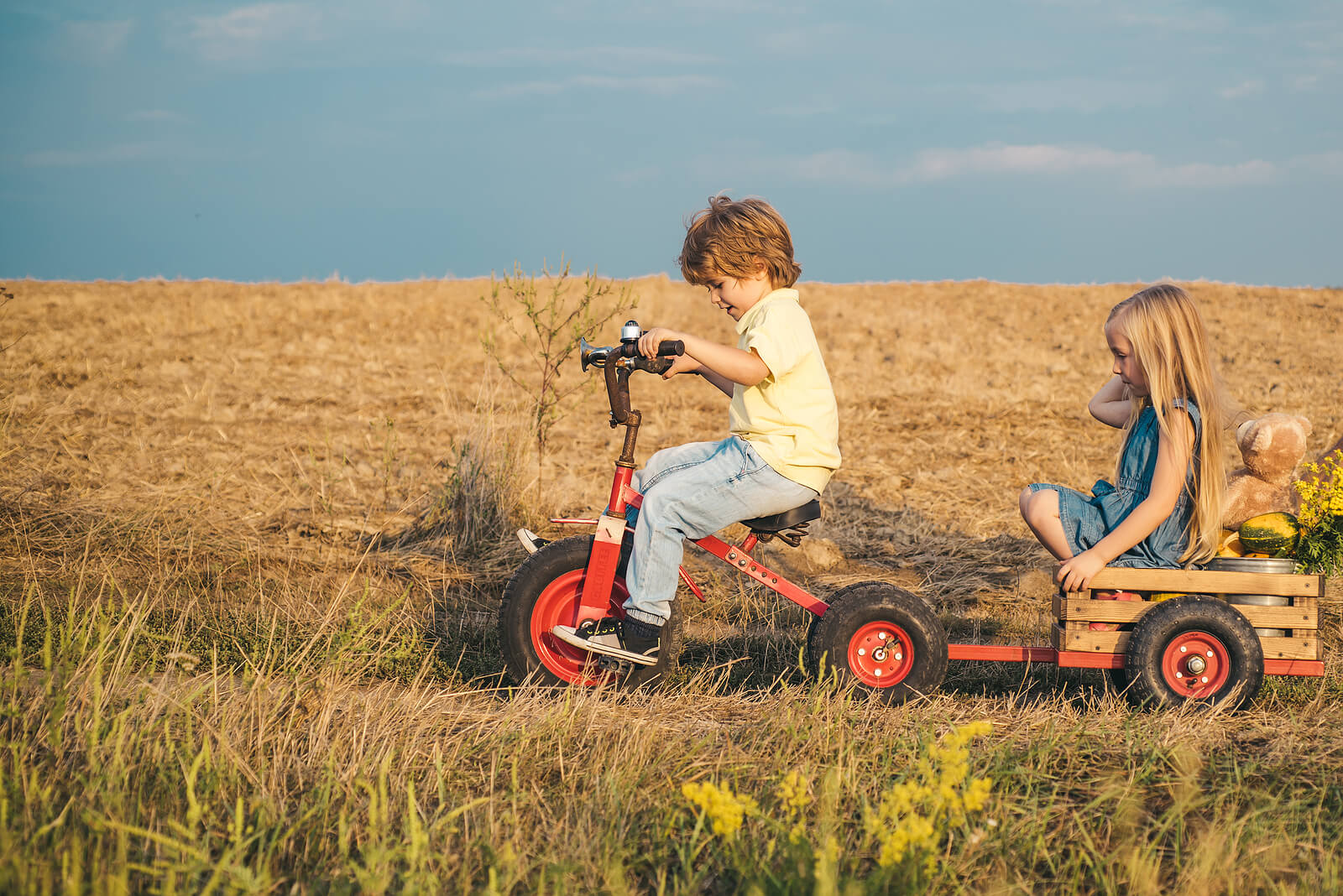 Amigos jugando por el campo con un triciclo a modo de tractor con remolque.