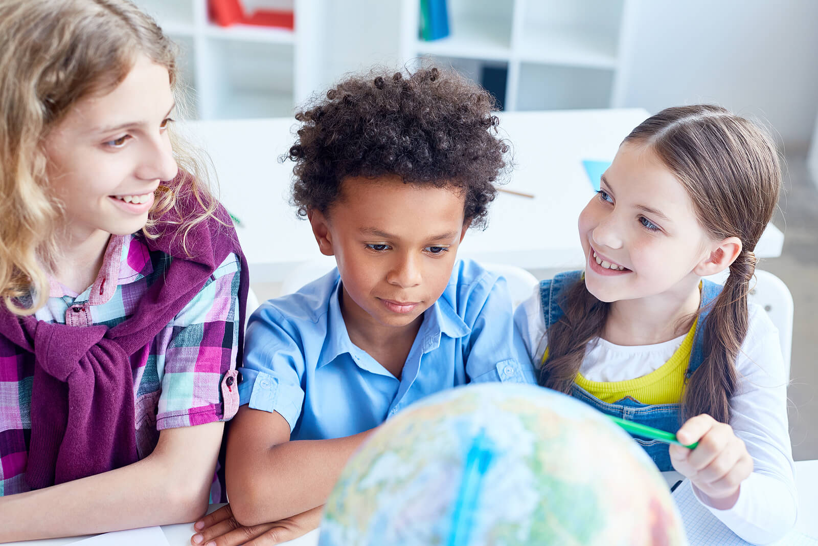Trois enfants qui regardent un globe terrestre. 