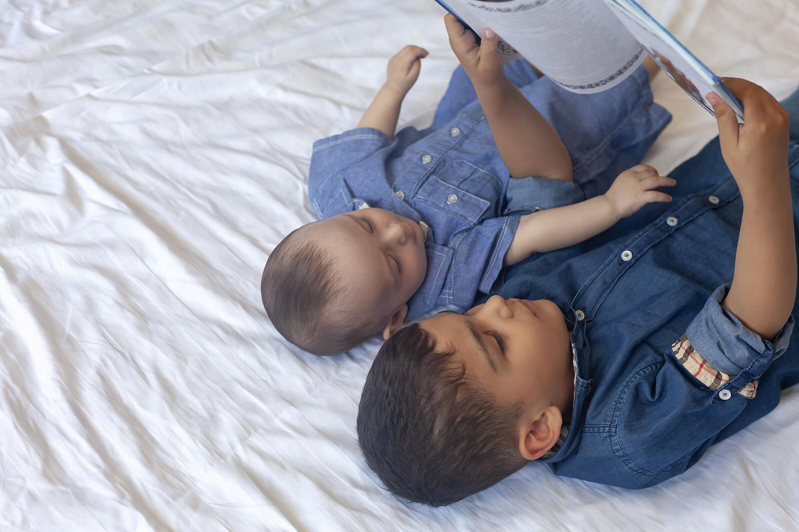 Hermanos leyendo cuentos sobre la envidia tumbados en la cama.