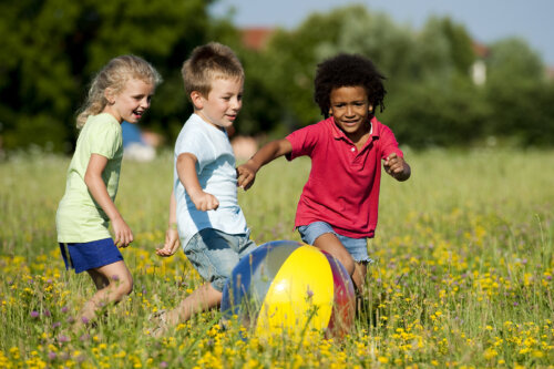 Niños jugando con la pelota al aire libre en verano, uno de los hitos de desarrollo físico.