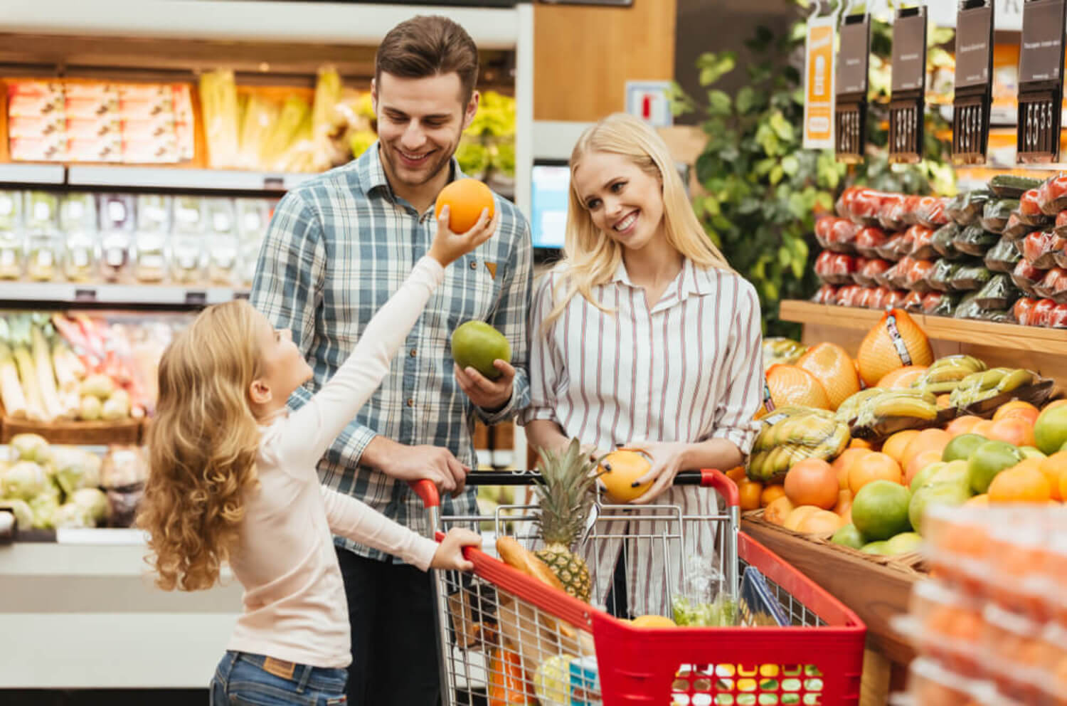 Padres comprando fruta en el supermercado con su hija para que aprenda matemáticas.