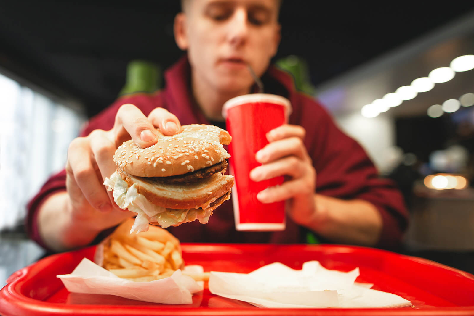 Adolescente che mangia un hamburger in una catena di fast food.