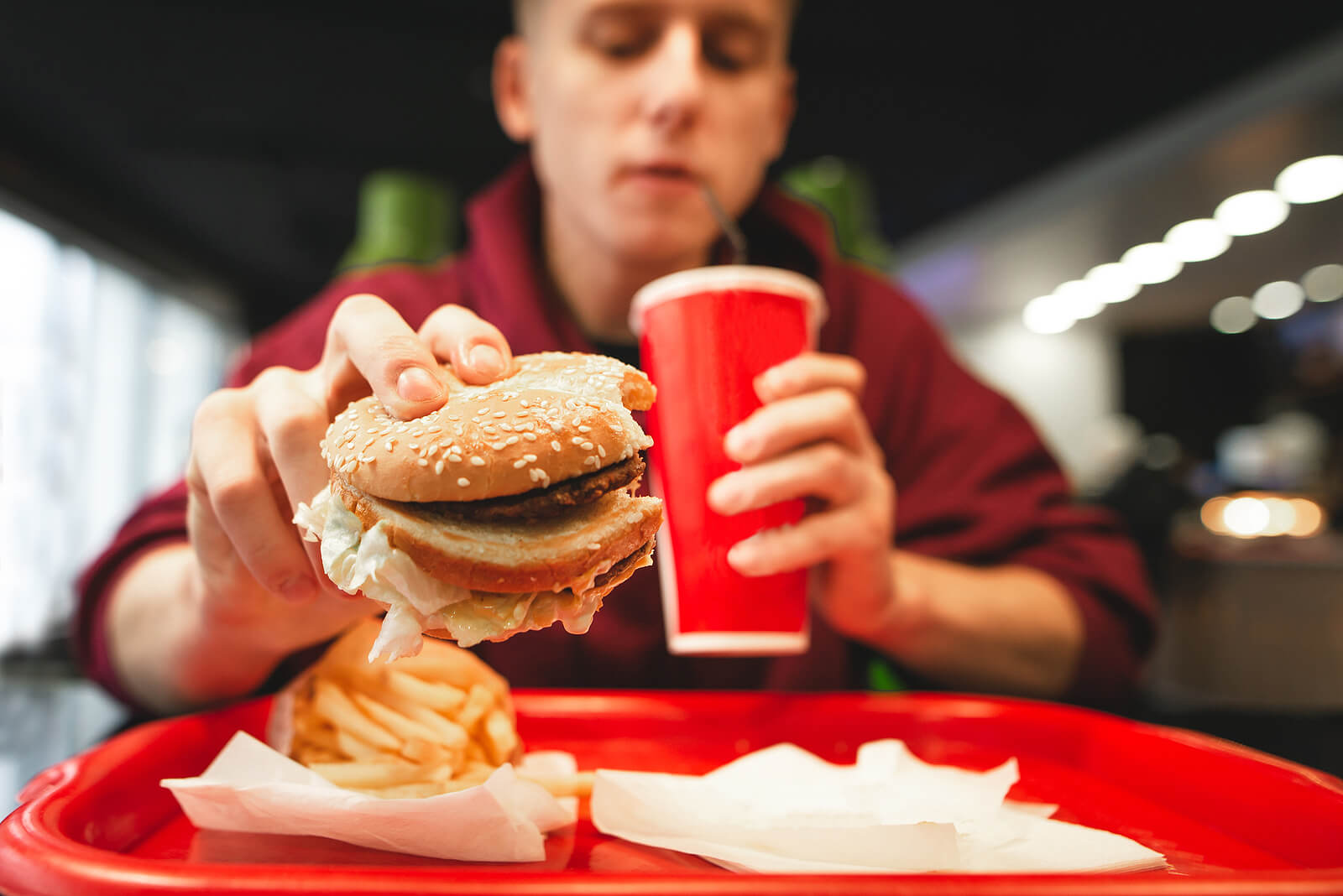 Un adolescent qui mange un hamburger avec un soda;