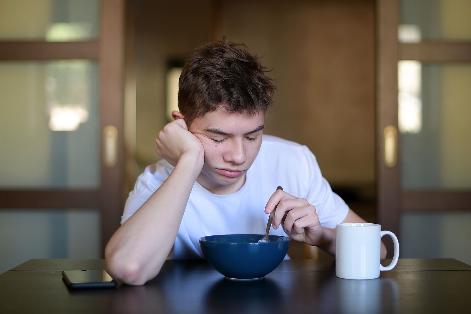 Adolescente desayunando con mucho sueño debido a que sufre el síndrome de fatiga crónica.