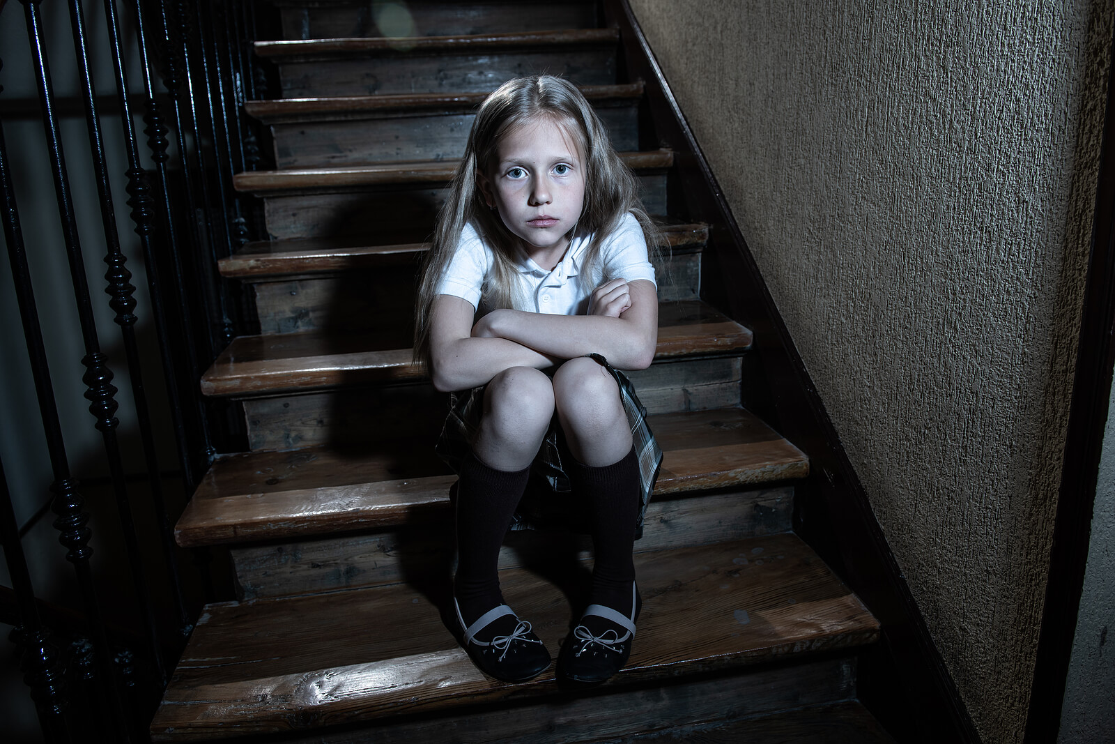 Niña sentada en la escalera de casa con el uniforme de la escuela porque no quiere ir al colegio.