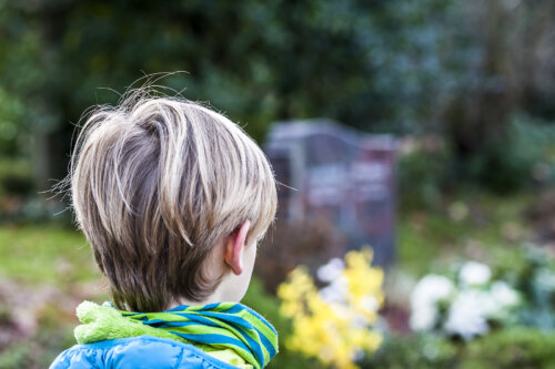 Niño en un cementerio visitando la tumba de un familiar.