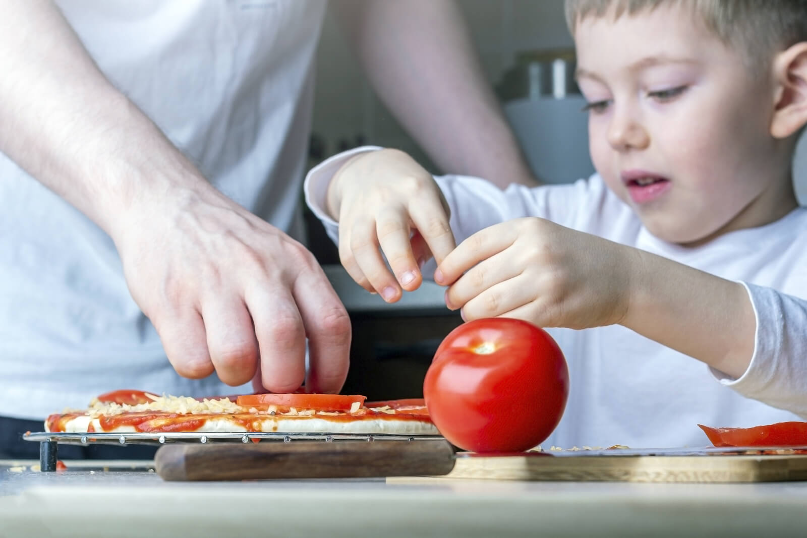 Niño ayudando a su padre a cocinar una pizza.