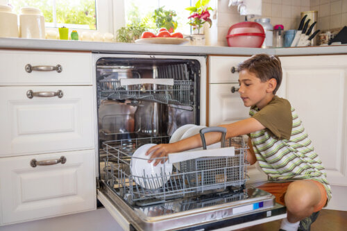 Niño metiendo los platos sucios en el lavavajillas.