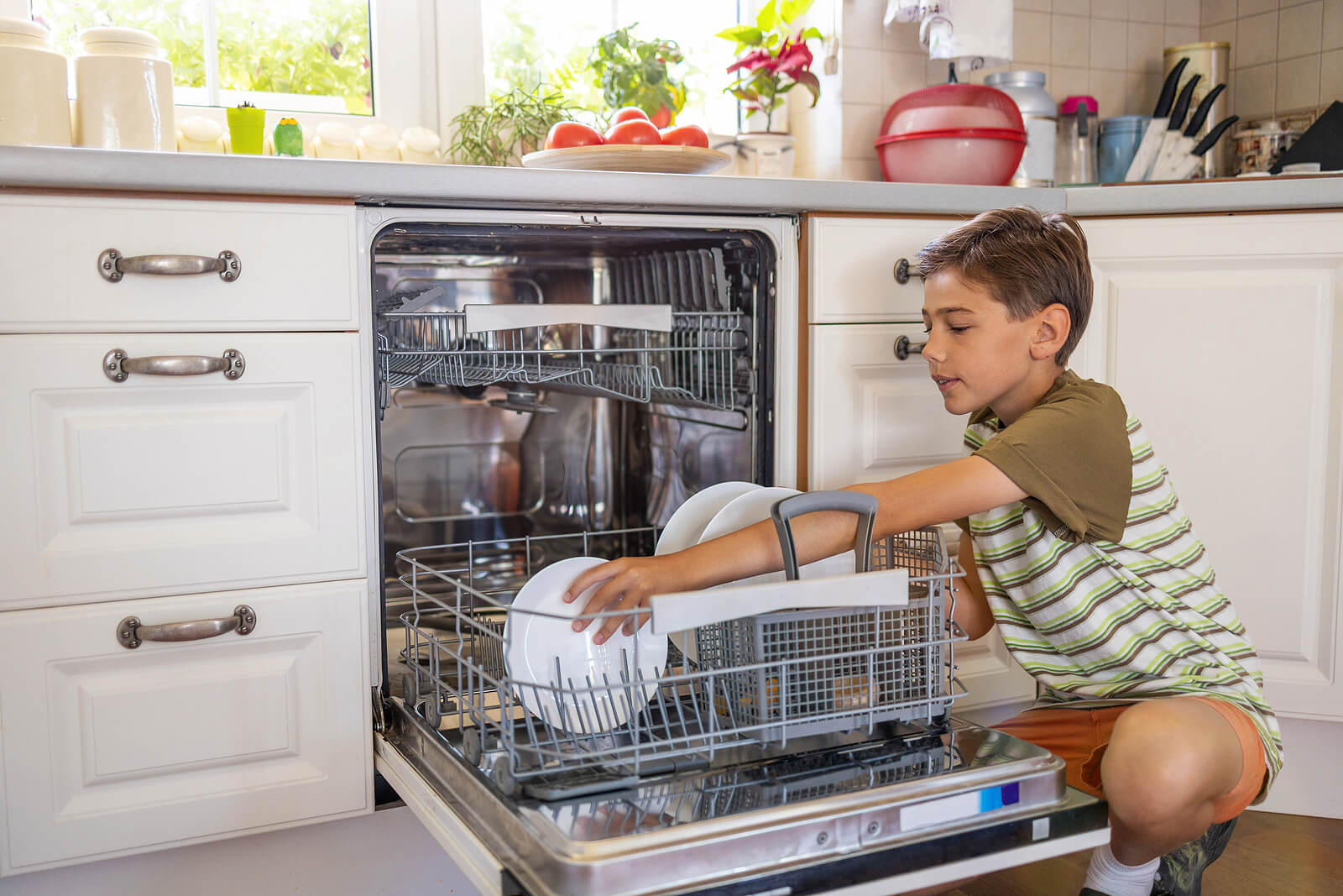 Niño metiendo los platos sucios en el lavavajillas para fomentar la responsabilidad en niños.