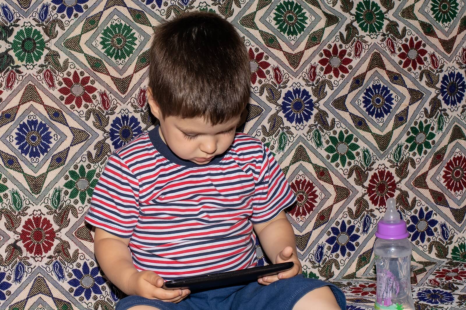 Bambino che guarda film sul cellulare perché non è in grado di disconnettersi dagli schermi.