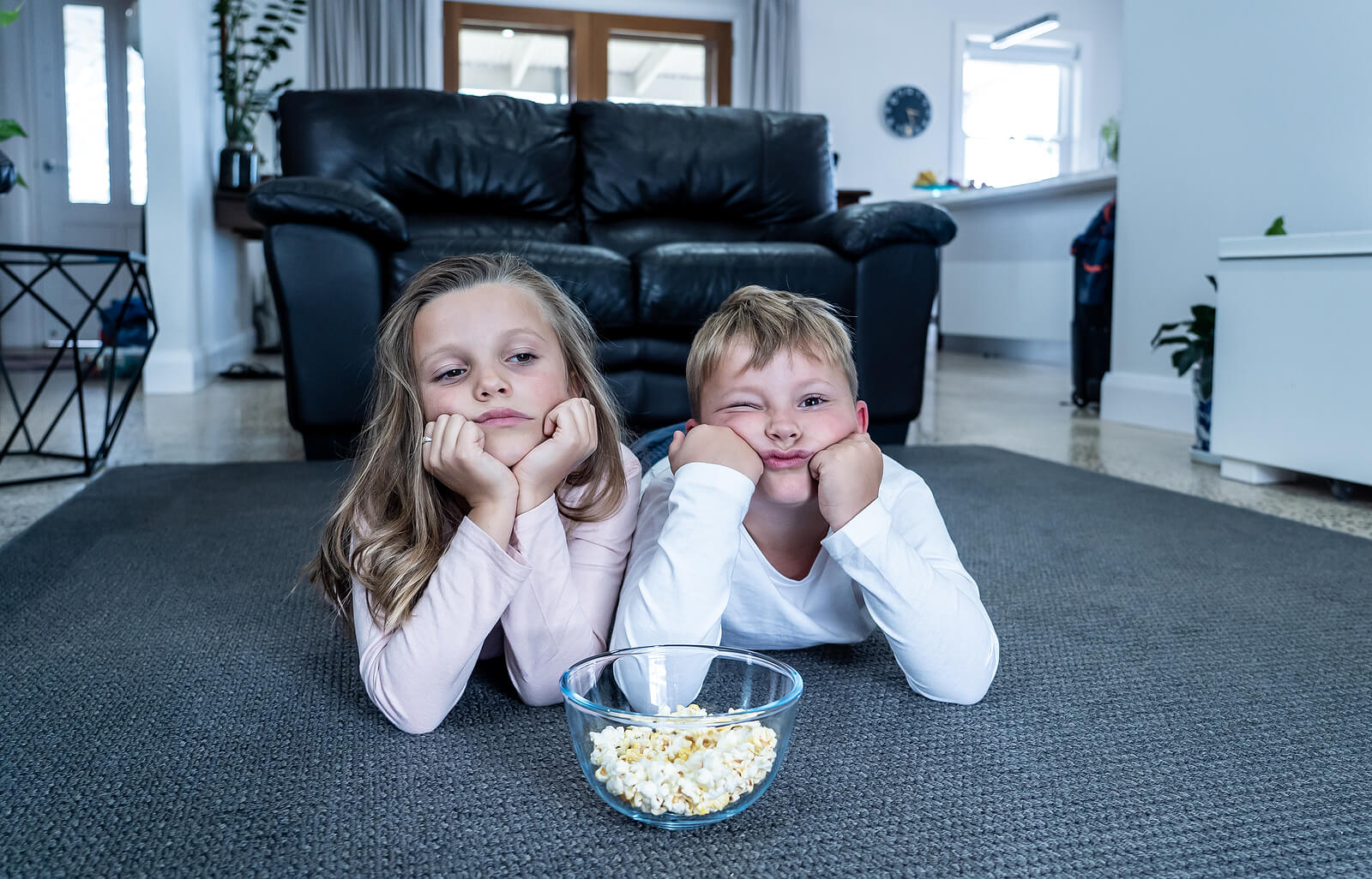 Niños aburridos viendo la televisión y comiendo palomitas.