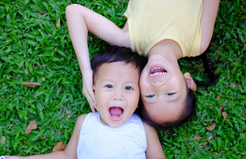 Niños tumbados muy sonrientes en la hierba pensando en nombres de bebés.