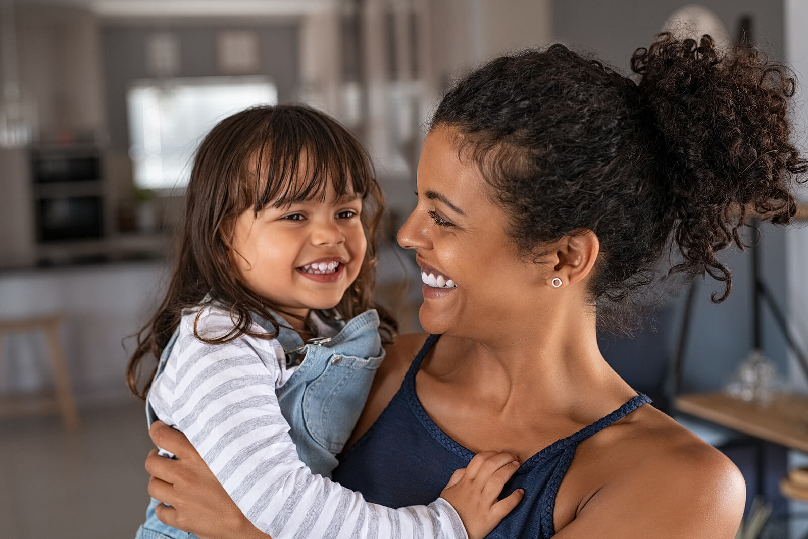 A mother holding her toddler daughter and smiling.