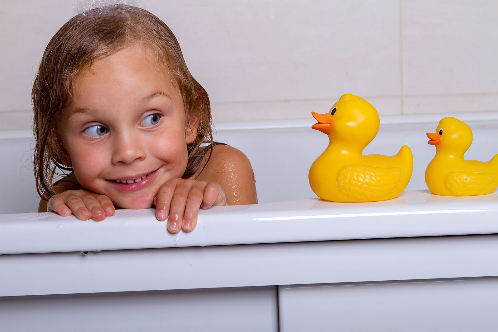 Niña jugando con los patitos de goma en la bañera.