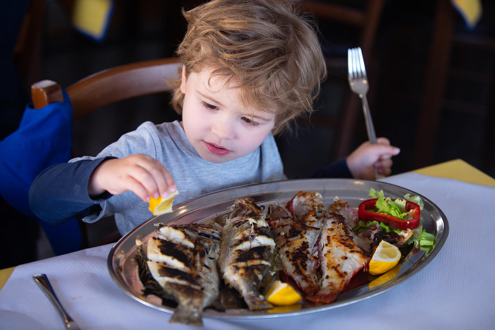 A child squeezing lemon onto grilled fish.