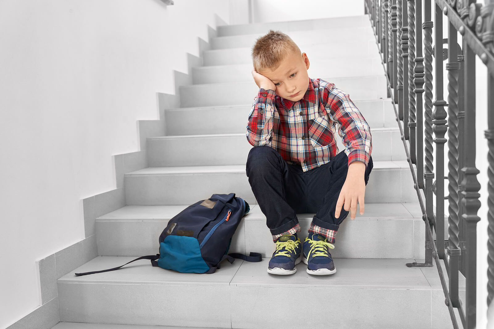 Niño sentado en las escaleras de casa pensando en que tiene que ir al colegio pero sufre fobia escolar.