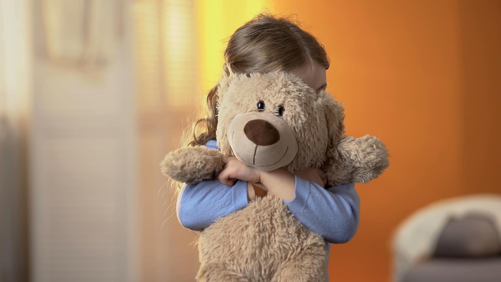 Niña abrazando un osito de peluche porque tiene miedo.