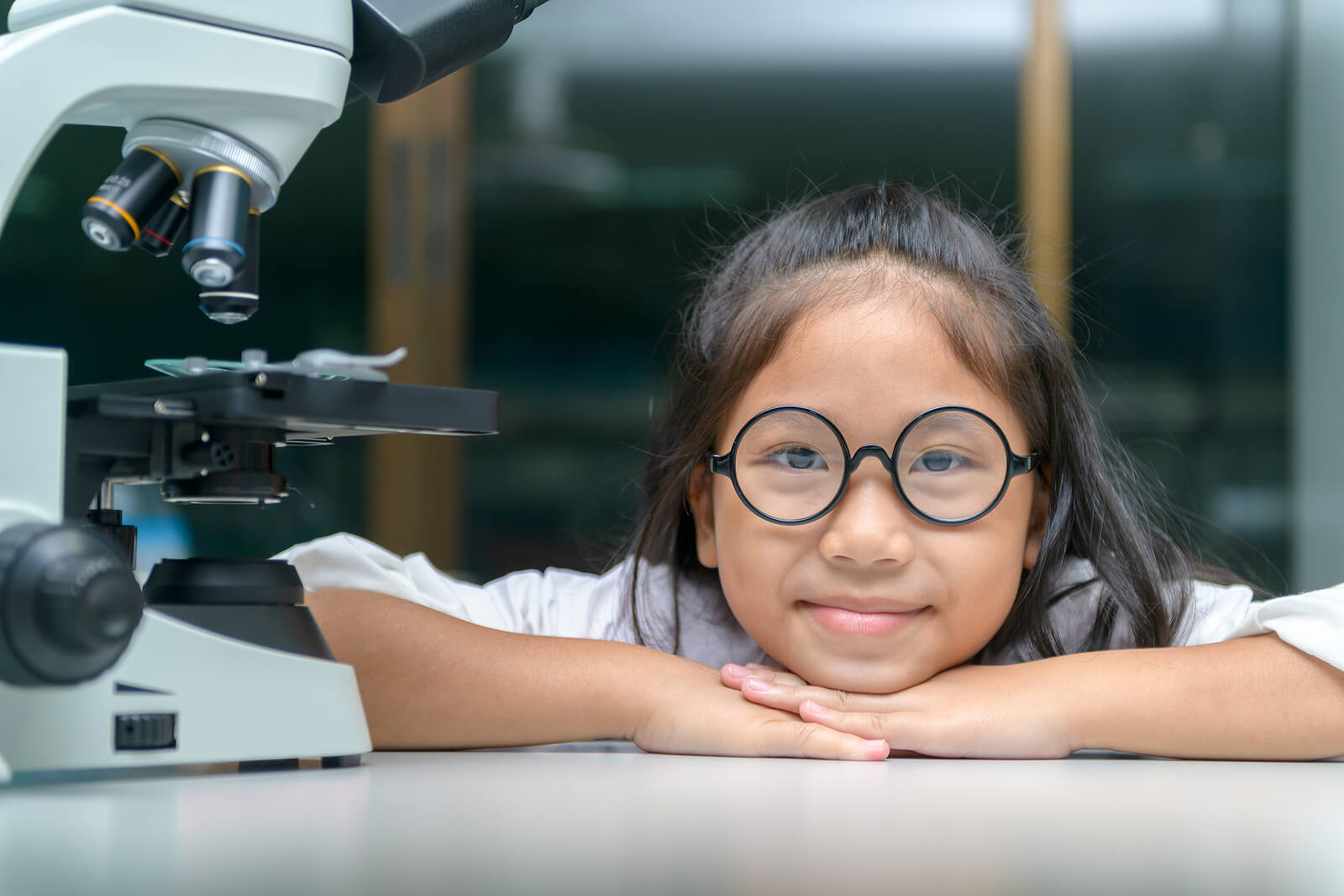 Niña científica junto a un microscopio.