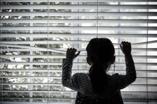 Niña mirando por la ventana muy triste.