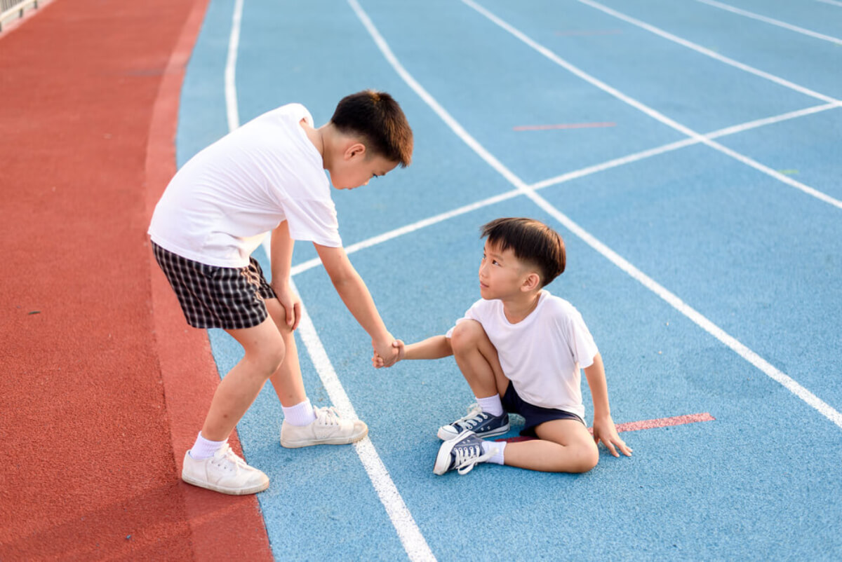 Un enfant qui aide un autre à se relever sur un terrain d'athlétisme.