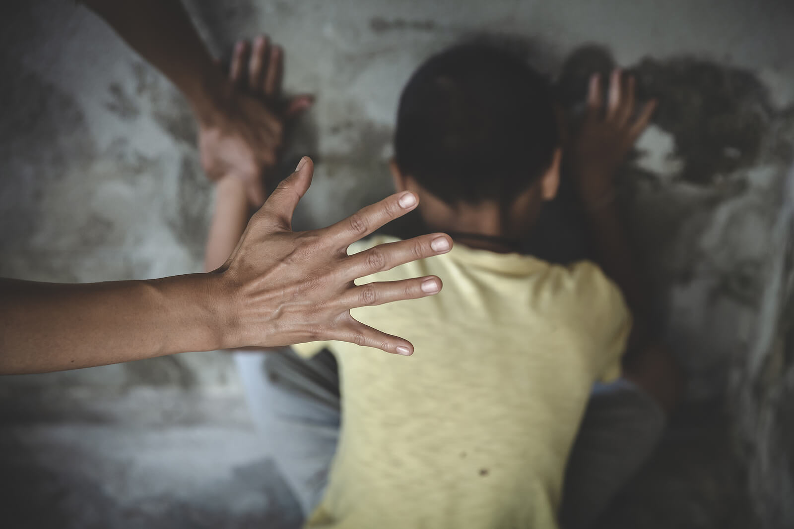 A woman's hand preparing to hit a child who's crouched down on the floor.