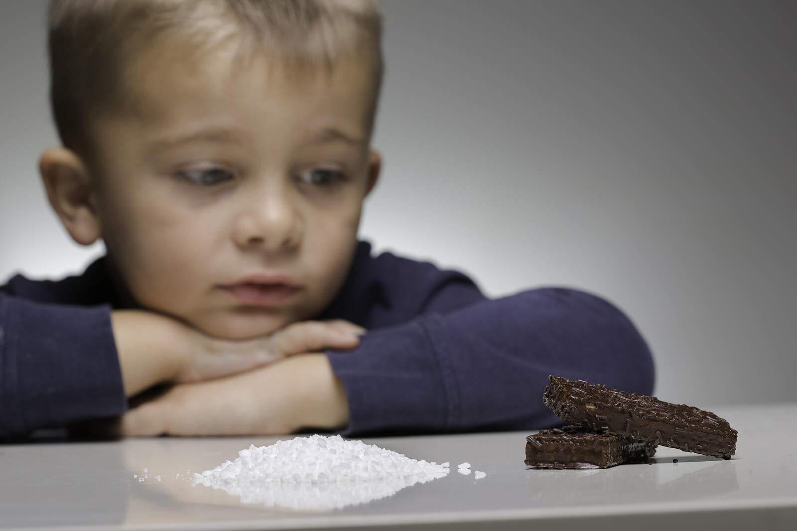 Niño mirando una montaña de azúcar y un trozo de chocolate.