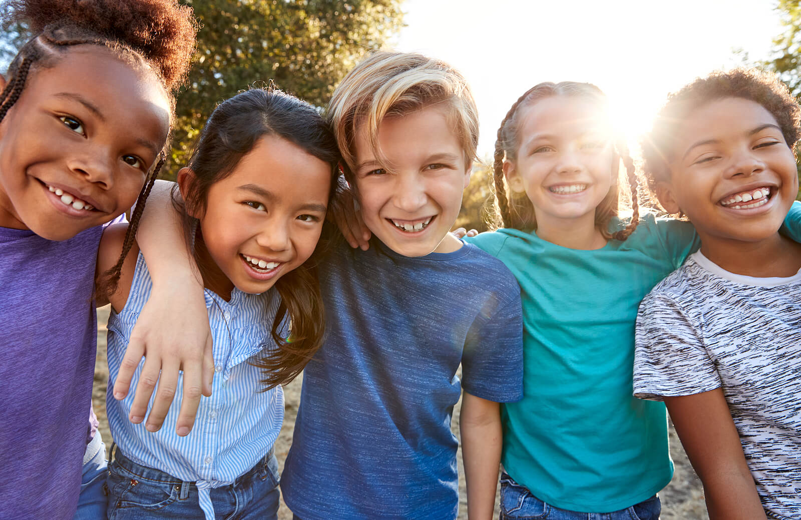 A diverse group of children smiling with their arms around one another.