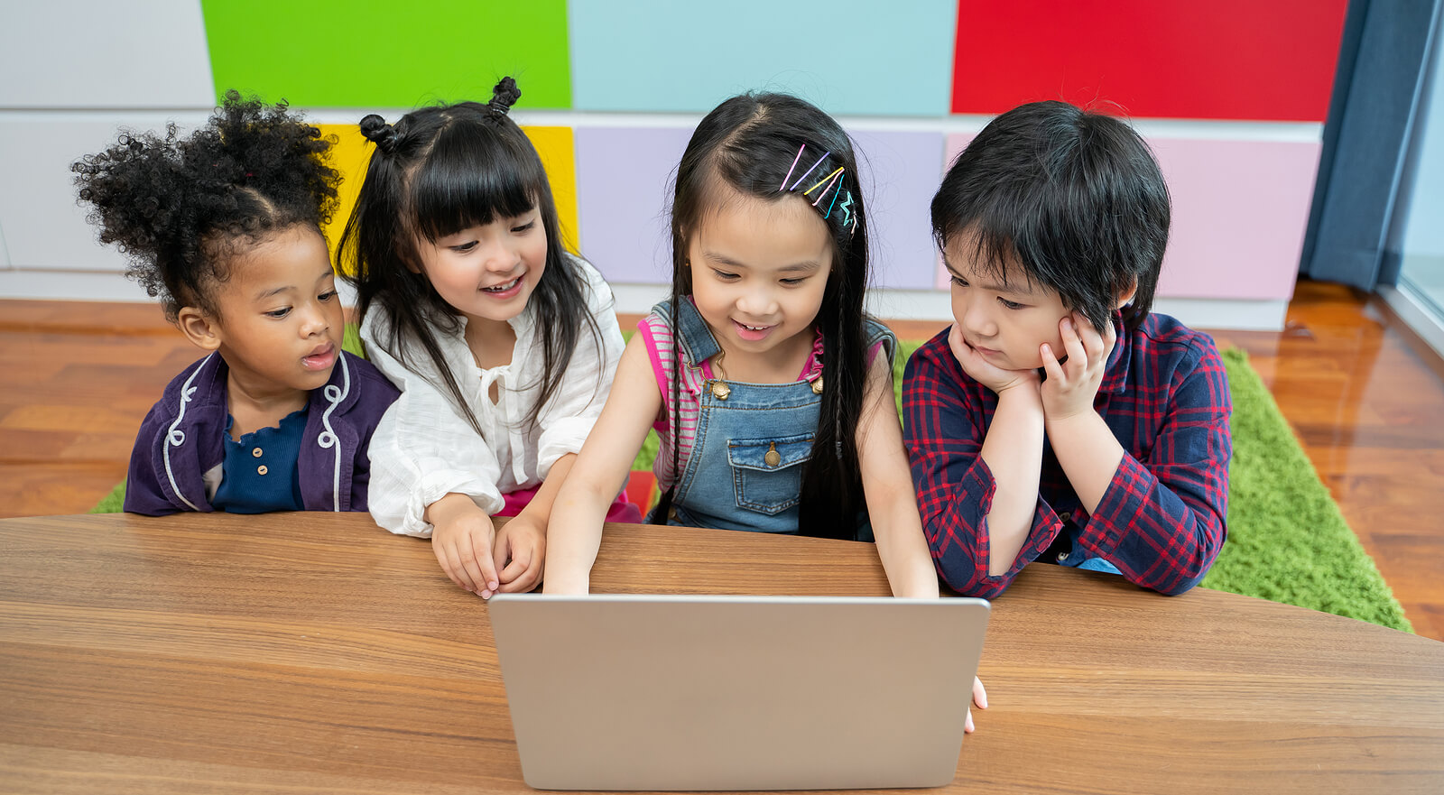 Four children sitting at a table looking at a laptop.