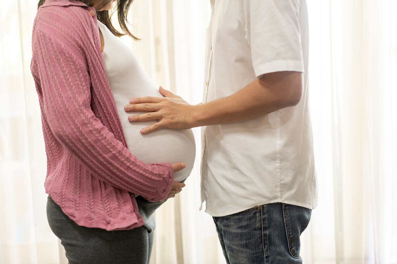 Une femme enceinte et son conjoint qui touche son ventre.