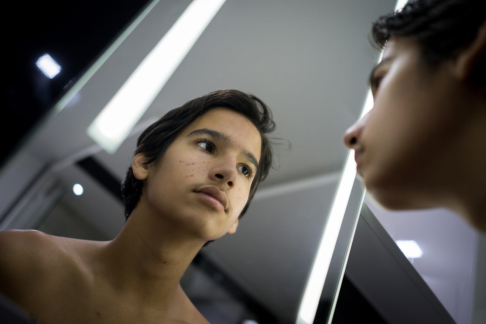 Chico adolescente mirándose al espejo porque sufre trastorno dismórfico corporal.