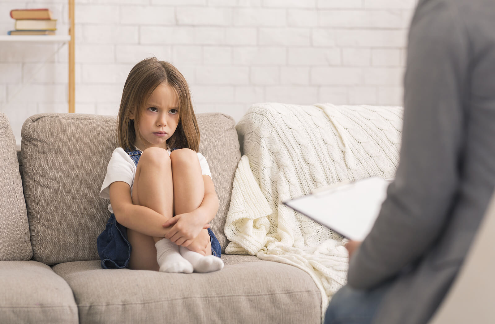 Niña enfadad sentada en el sofá porque su madre la ha regañado.