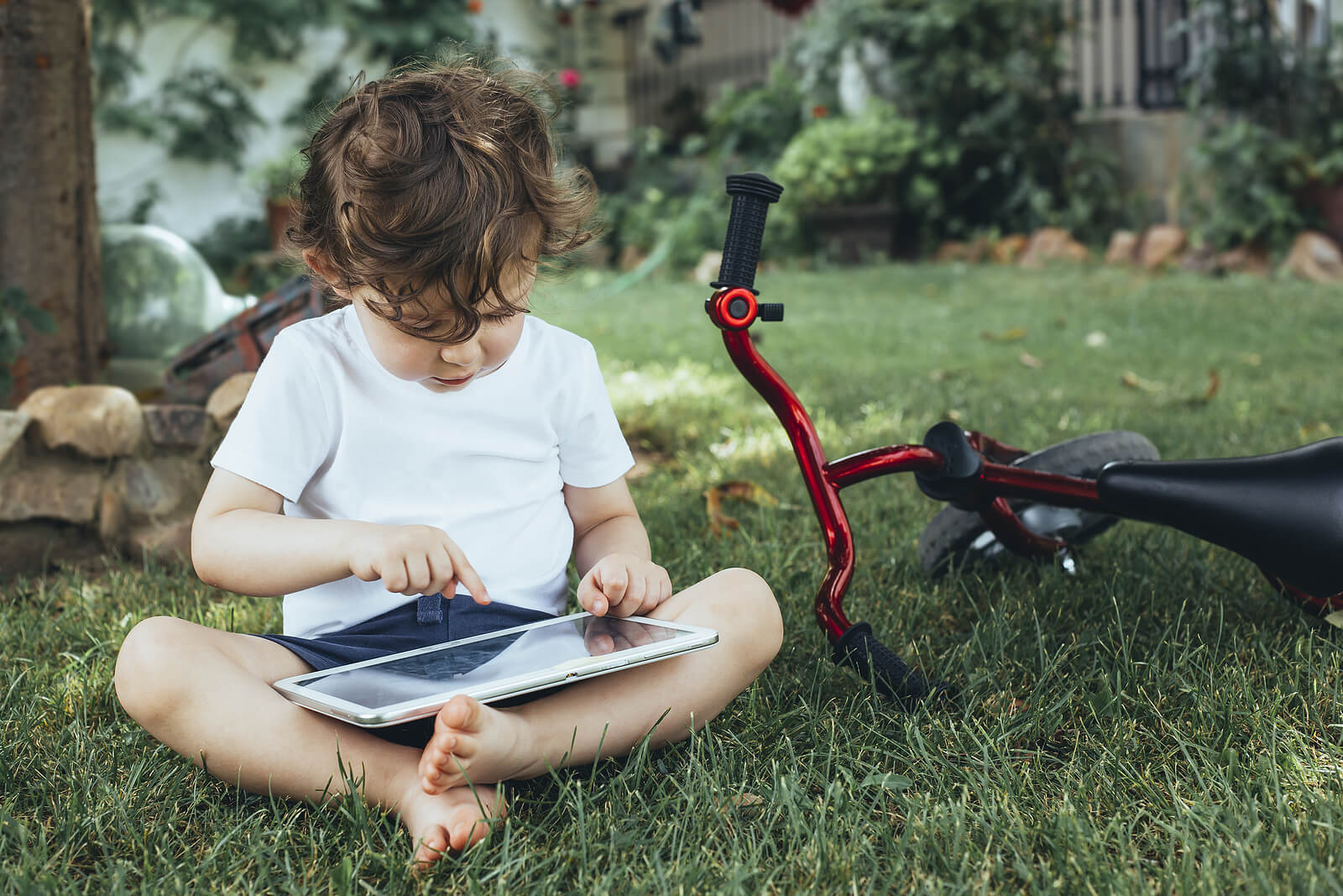 Niño jugando con una tablet junto a su bicicleta.