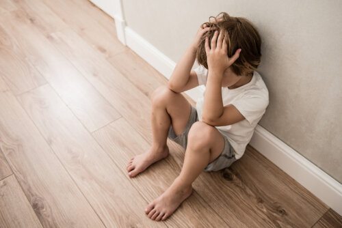 Niño llorando sentado en el suelo debido a la violencia familiar que sufre en casa.