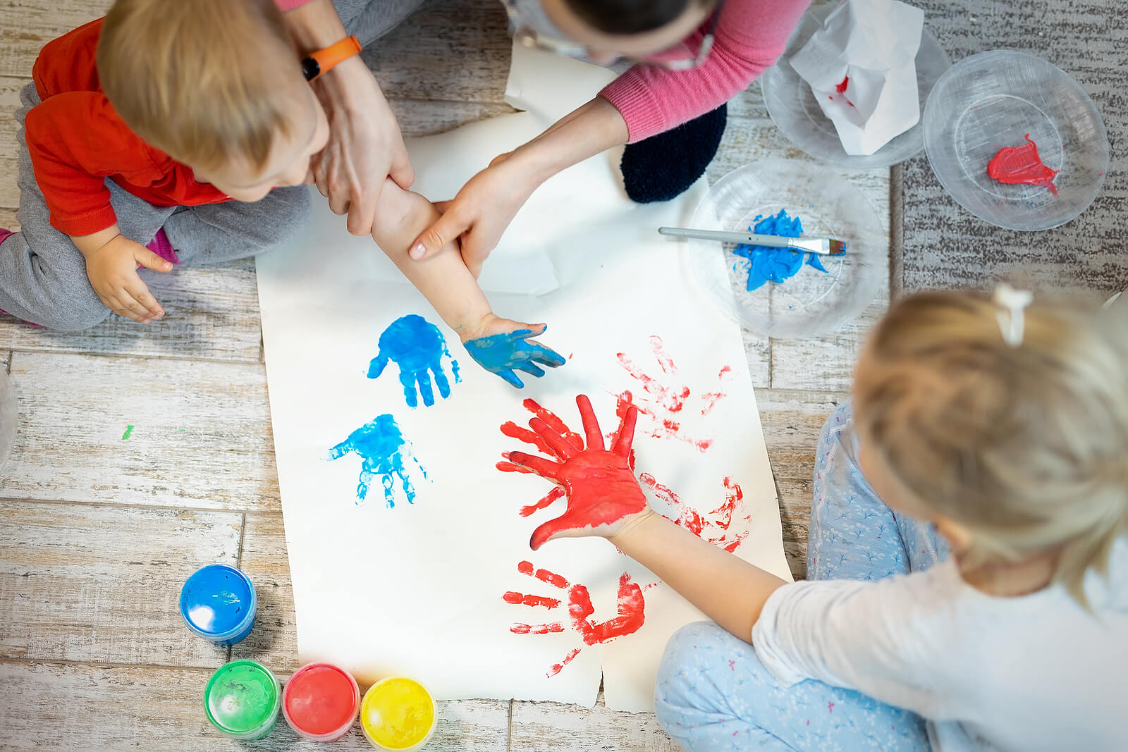 Madre con i suoi bambini che giocano a dipingere un murale con le dita e le mani.